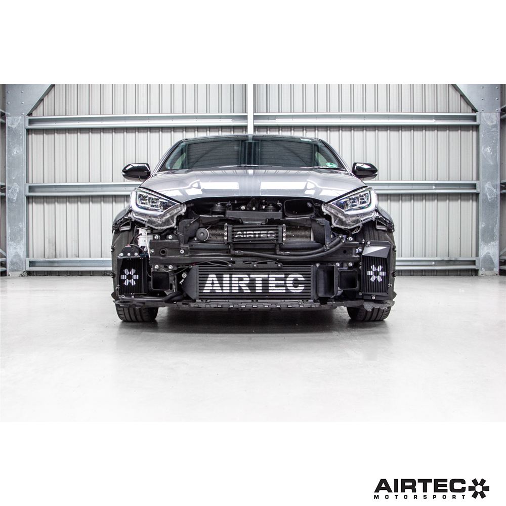 AIRTEC Motorsport auxiliary radiator installed in a Toyota Yaris GR Gen2; black metal core with hoses connected.