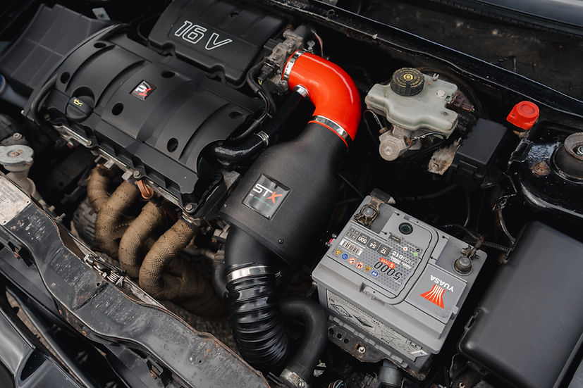 SprogTech STX TU5 enclosed intake kit for Peugeot 106 and Citroen Saxo, shown installed on the engine bay with sleek black tubing.