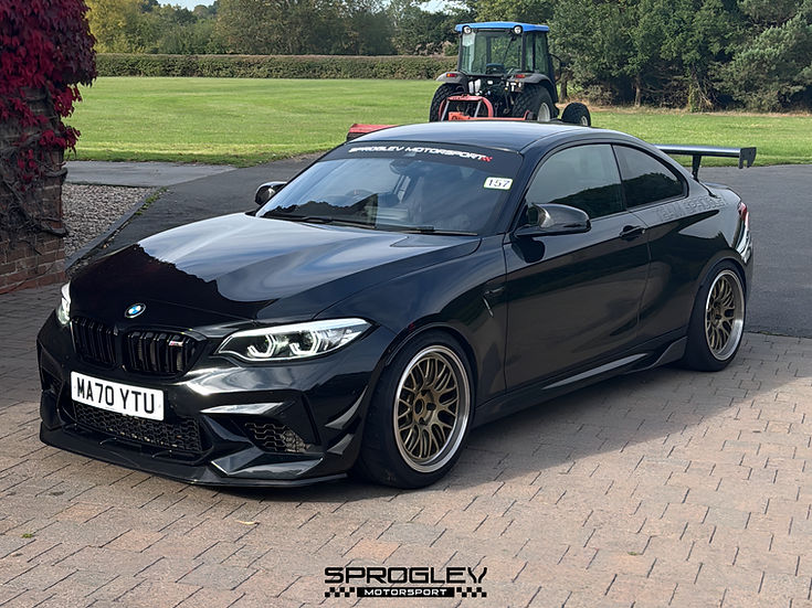 Sprogley Motorsport front bumper canards for F87 BMW M2, aerodynamic body styling components on a black car.